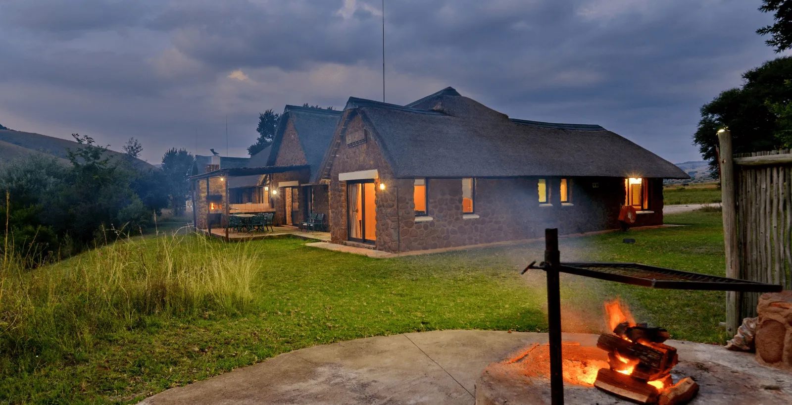 Stone chalet with thatched roof at dusk | Doornkop Resort - Mpumalanga - Carolina - Doornkop trout dams